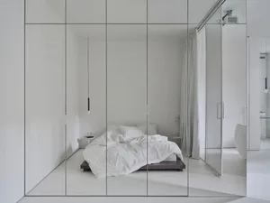 A minimalist bedroom with a white bed and white walls.