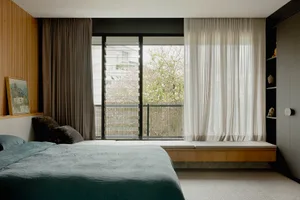 Modern minimalist bedroom featuring a floating bed, wooden headboard, and white sheer curtains framing a large window.