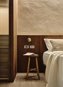 Minimalist bedroom featuring wood furniture and cement walls with a stool and book as focal points.