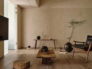Minimalist living room with wooden tables and floor, black armchair, and simple decoration.