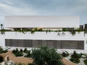 White marble residential building with greenery on the roof and ground floor.