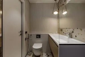 Modern bathroom with white terrazzo floor tiles and wall panels, white toilet, white countertop, and single sink.