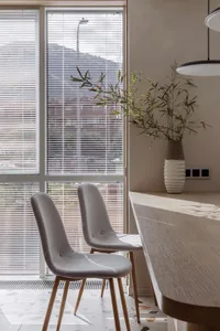 Two minimalist grey chairs sit at a dining table with a vase of greenery in a modern interior design living space.
