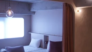 Minimalist bedroom with concrete walls, white bedding, and purple accent pillows.