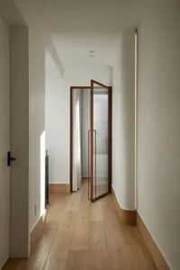 A minimalist corridor with wooden flooring, taupe-colored walls, and glass details.