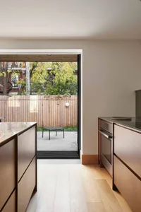 Modern, minimalist kitchen with wooden cabinets, glass countertop, and outdoor view through large window.