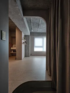A minimalist residential space featuring exposed concrete walls and a large window.