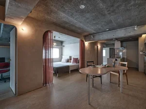 A minimalist apartment with concrete walls, a dining table, and a bedroom area with a bed.