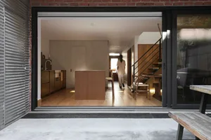 A modern minimalist kitchen with wooden furniture, featuring a central wooden island and a bar stool.