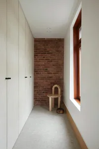 A minimalist interior design featuring a brick wall and wooden chair in a narrow corridor.