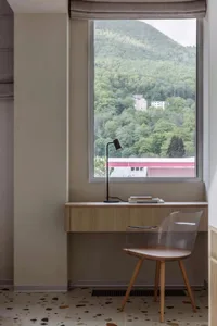 A minimalist work station featuring wooden elements and a lamp on a window sill, with a scenic mountain view outside.