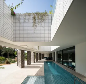 A modern residential house with concrete walls and a pool, featuring plants and a spacious interior.