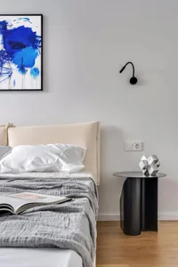 A modern bedroom with a beige bed and a metal side table with a geometric sculpture on top.