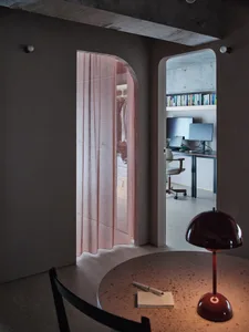 A modern home office with a pink curtain, computer desk, and bookshelf.