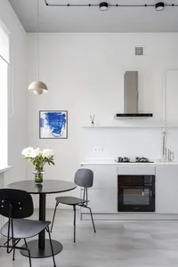 現代簡約廚房，白色牆面搭配黑色餐桌、餐椅，以及一瓶白色花卉。