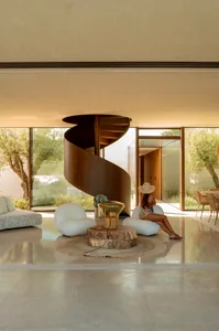 A modern minimalist living room with a spiral staircase, concrete floor and walls, and natural light.