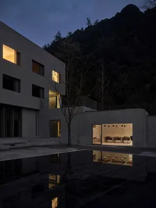 A modern residential interior with concrete walls and floors, featuring a large open space with a dining and seating area.