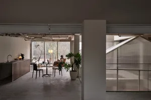 Modern minimalist living dining space with concrete floors, glass walls, and wooden furniture.