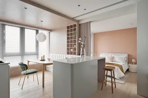 A modern, minimalist kitchen with white countertops, wooden chairs, and a white pendant light hanging from the ceiling.