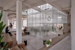 A modern indoor coworking space featuring concrete walls and a glass partition.