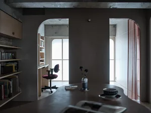 A modern minimalist home office features a concrete wall with an arched doorway leading to a wooden desk.