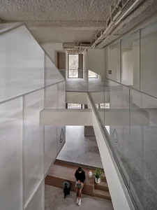A modern office space with concrete floors and walls, featuring a glass partition and a person working on a laptop.