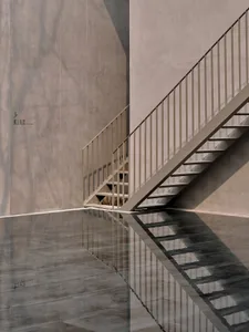 A concrete staircase with a metallic handrail reflected in a glossy floor.