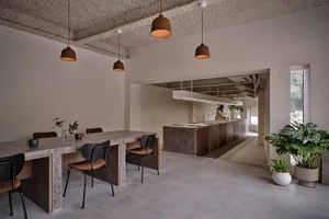 Minimalist cafe interior with concrete walls, wood furniture, and hanging pendant lights.