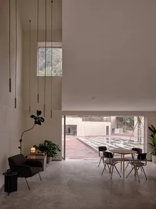 Minimalist living room featuring concrete pendant lights, a black armchair, and a dining table with chairs.