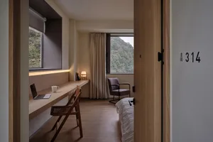 A spacious, modern bedroom with wood furniture, a fabric-covered chair, and a bed with a white duvet, featuring a large windo
