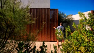 A man standing at the entrance of a modern garden with a wooden fence and green foliage.