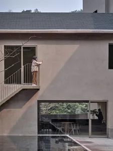 A modern residential house with concrete walls and a glass door, featuring a balcony and a courtyard.