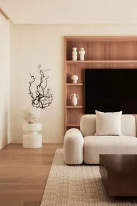 A minimalist living room with a wooden print on the back wall, white couch, and abstract sculpture.