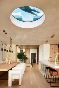 Modern dining room with wood floors and white chairs, designed with a glass ceiling showing a swimmer in a pool.