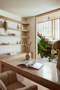 A modern home office featuring a wooden desk with a marble top, surrounded by minimalist shelves and a large potted plant.