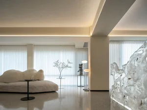 Modern minimalist living room featuring glass and metal elements and white, vertical blinds allowing natural light in.