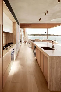 A modern residential kitchen featuring wooden cabinets, a marble countertop, and a view of the ocean.