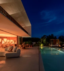 A modern residential patio with minimalist furniture and a large swimming pool under a dark, starry sky.