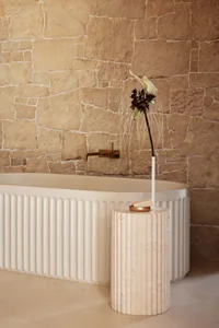 Modern bathroom with white marble bathtub and stone wall.