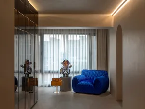 A modern blue armchair with a textured upholstery in a room with large windows and sheer curtains.