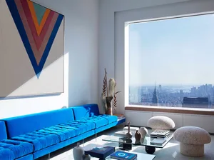 A living room with a blue sofa and a large window overlooking a cityscape.