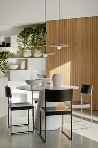 Modern dining room featuring a round white table, black metal chairs, and a wooden wall panel.