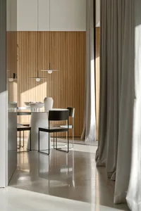 Modern dining room featuring a sleek, white round table and black chairs with a white vase and bowls on it, against a wooden-