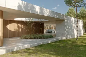 A modern carport with a concrete facade and a gravel driveway surrounded by grass and trees.