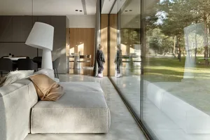 Modern living room interior with concrete flooring, minimalist furniture, and large windows allowing natural light to enter.