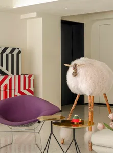 A modern living room with a purple fabric chair, a sheep sculpture, and a side table with a coffee cup and vase of pink tulip