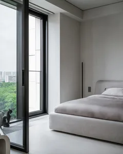 Modern minimalist bedroom featuring a grey upholstered bed with a fabric headboard, large window with urban view, and sleek d