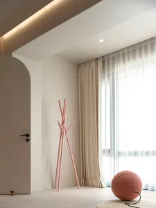 A minimalist living room with neutral colors, fabric curtains, and a metal coat rack.