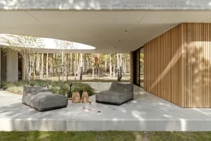 Concrete floor lounge area with modern furniture, surrounded by a natural forest setting.
