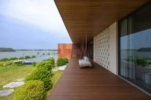 Modern residential terrace with wood floor, hanging swing, and concrete wall overlooking a lake.